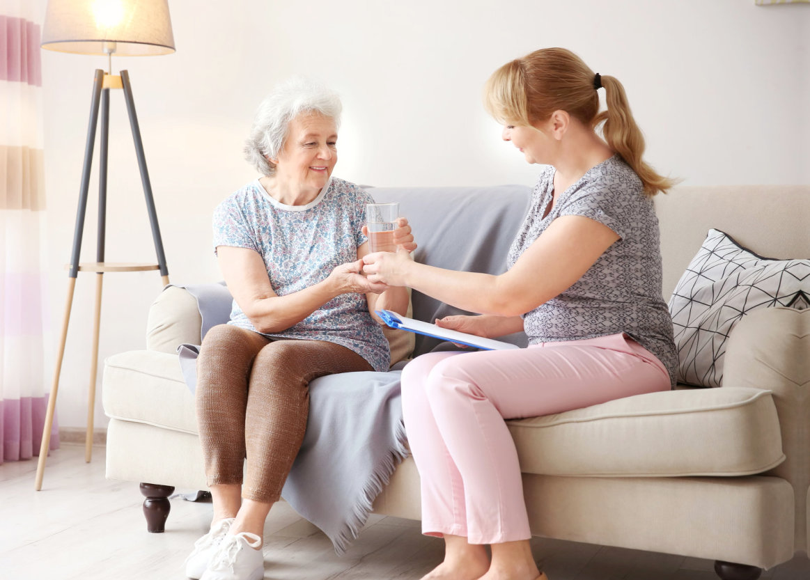 caregiver offering water to senior woman